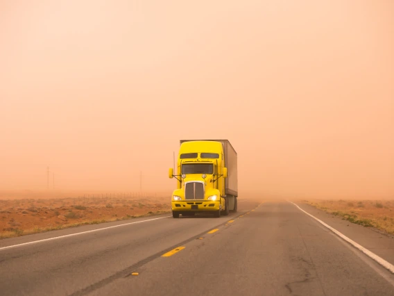 yellow semi truck driving through a dust storm